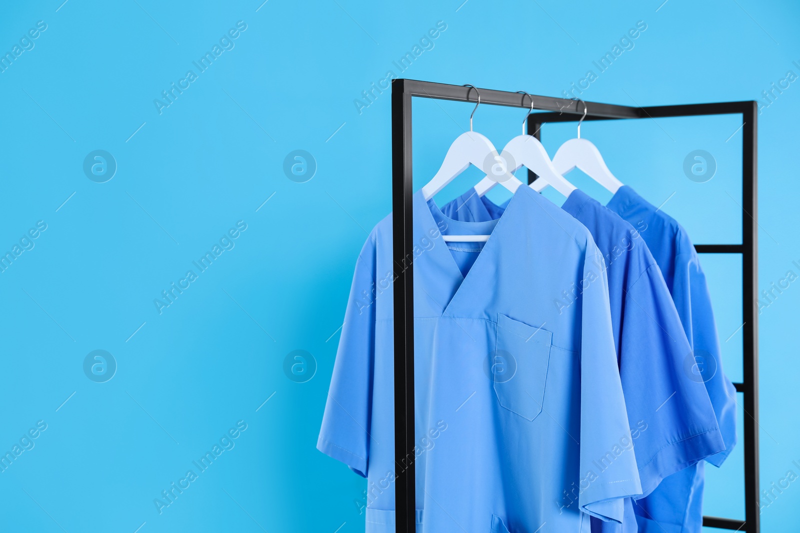 Photo of Medical uniforms on metal rack against light blue background. Space for text