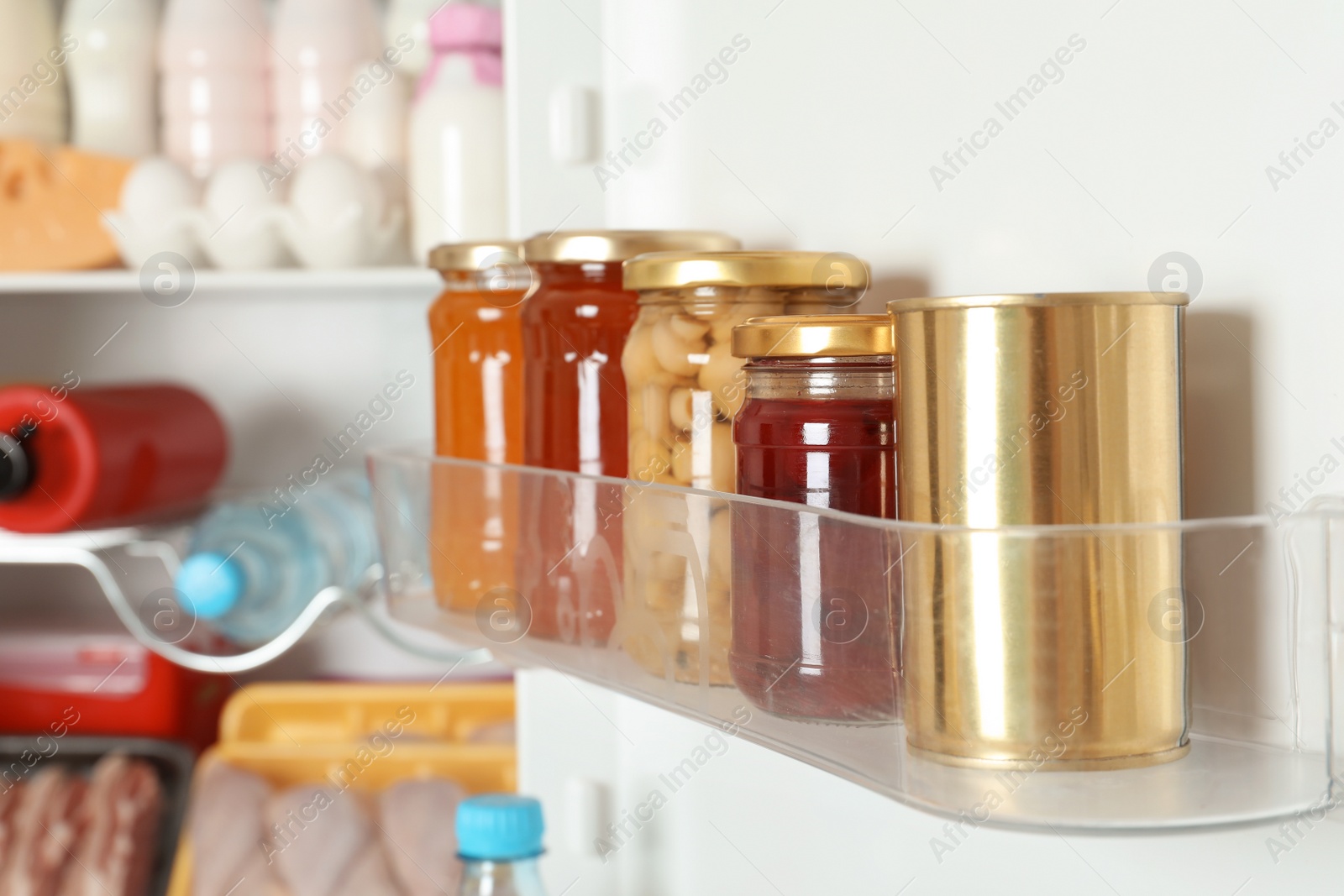 Photo of Jars with preserves and tin can on refrigerator door shelf, closeup