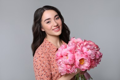 Beautiful young woman with bouquet of peonies on light grey background