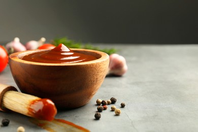 Photo of Tasty barbeque sauce in bowl, brush and peppercorns on grey textured table, closeup. Space for text