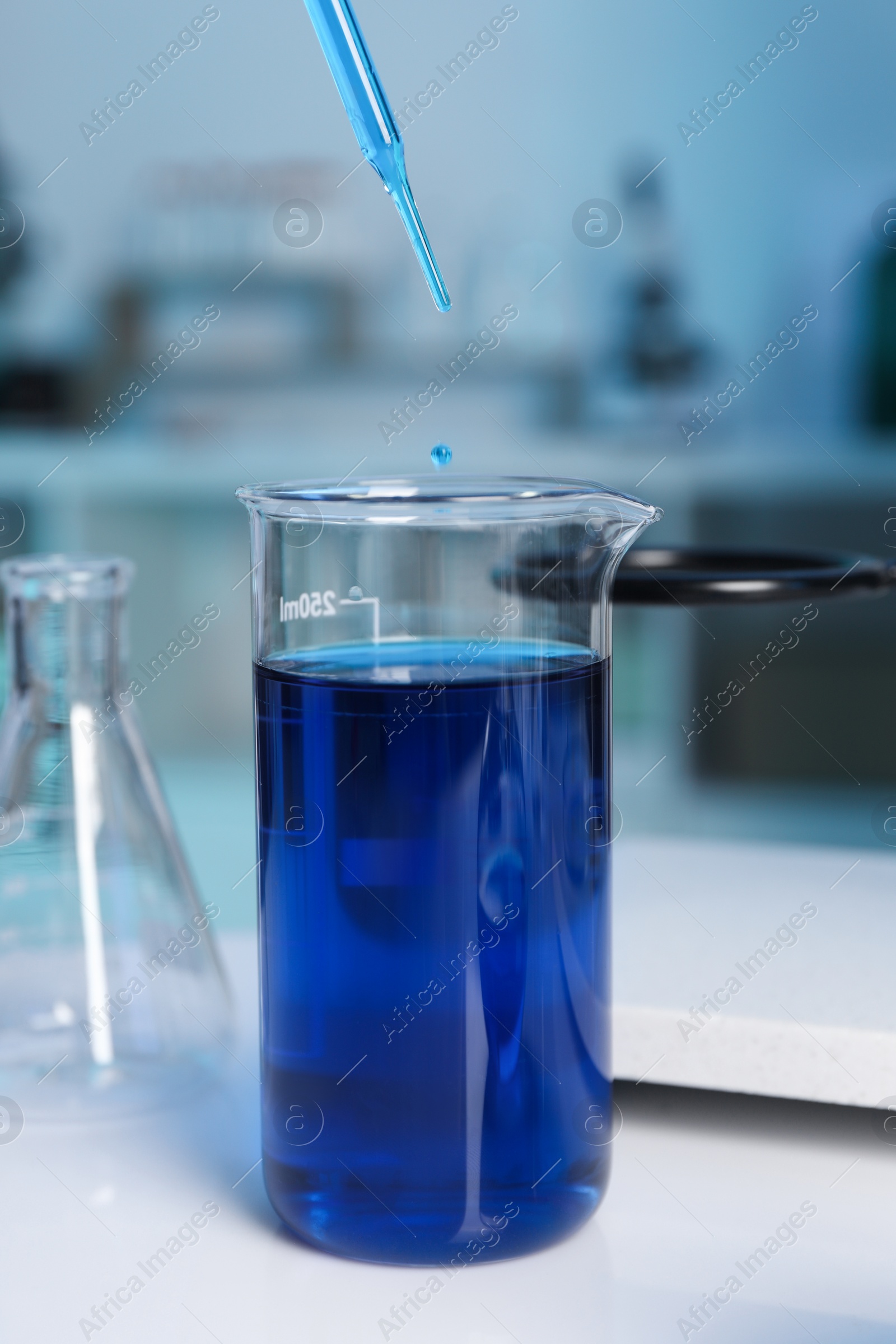 Photo of Laboratory analysis. Dripping blue liquid into beaker on white table, closeup