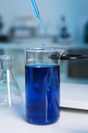 Photo of Laboratory analysis. Dripping blue liquid into beaker on white table, closeup