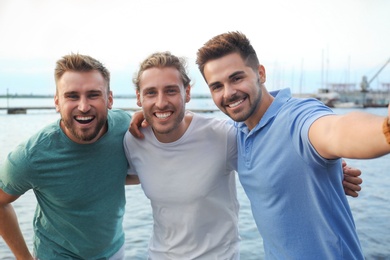 Happy young men taking selfie outdoors on sunny day