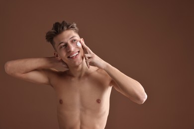 Photo of Handsome man applying moisturizing cream onto his face on brown background. Space for text