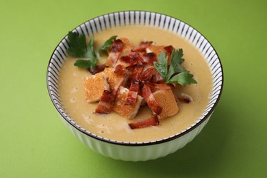 Photo of Delicious lentil soup with bacon and parsley in bowl on green table, closeup