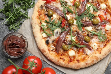 Photo of Tasty pizza with anchovies and ingredients on grey table, flat lay