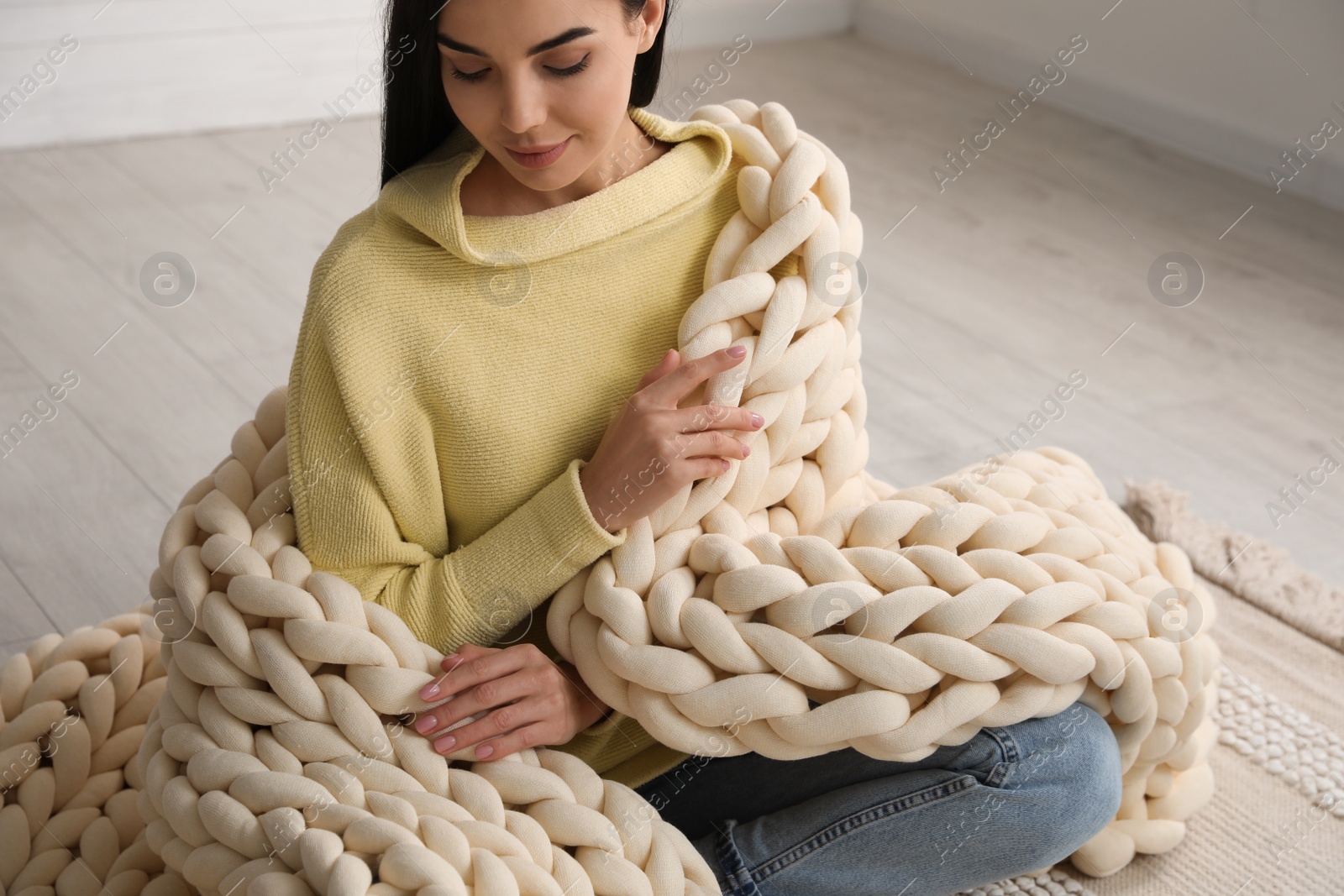 Photo of Young woman with chunky knit blanket on floor at home