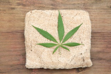 Photo of Hemp cloth and green leaf on wooden table, top view