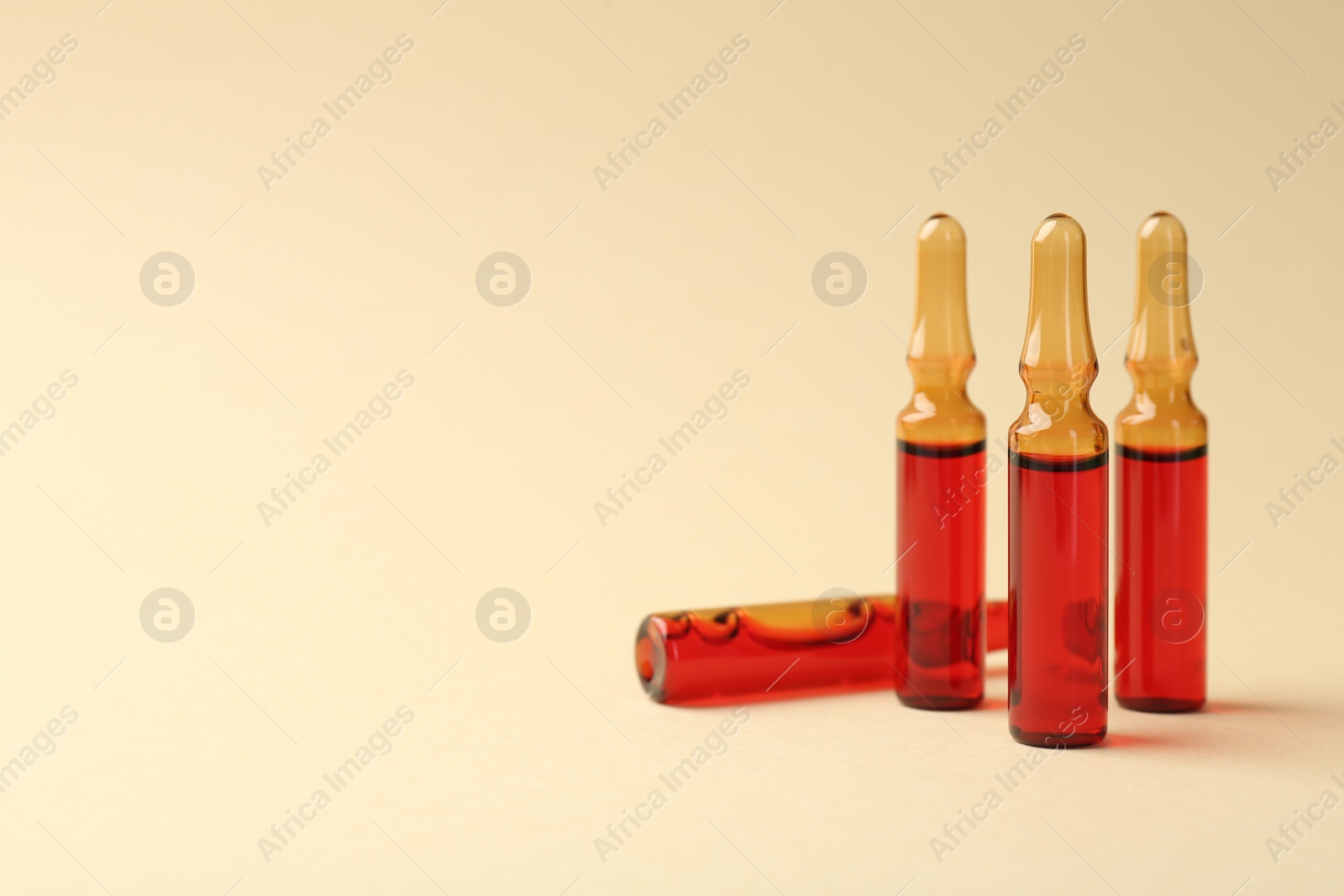 Photo of Glass ampoules with liquid on beige background. Space for text