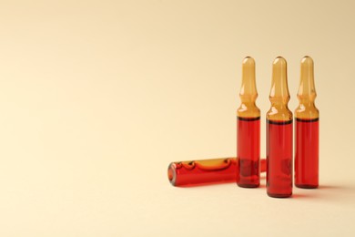 Photo of Glass ampoules with liquid on beige background. Space for text