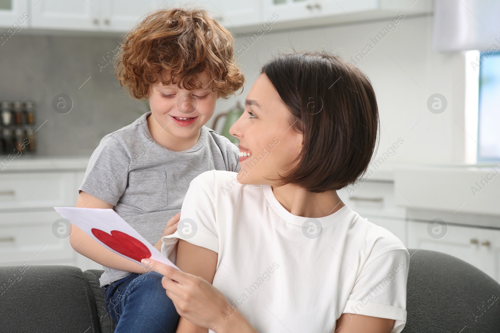 Photo of Little son congratulating his mom with Mother`s day at home. Woman holding greeting card