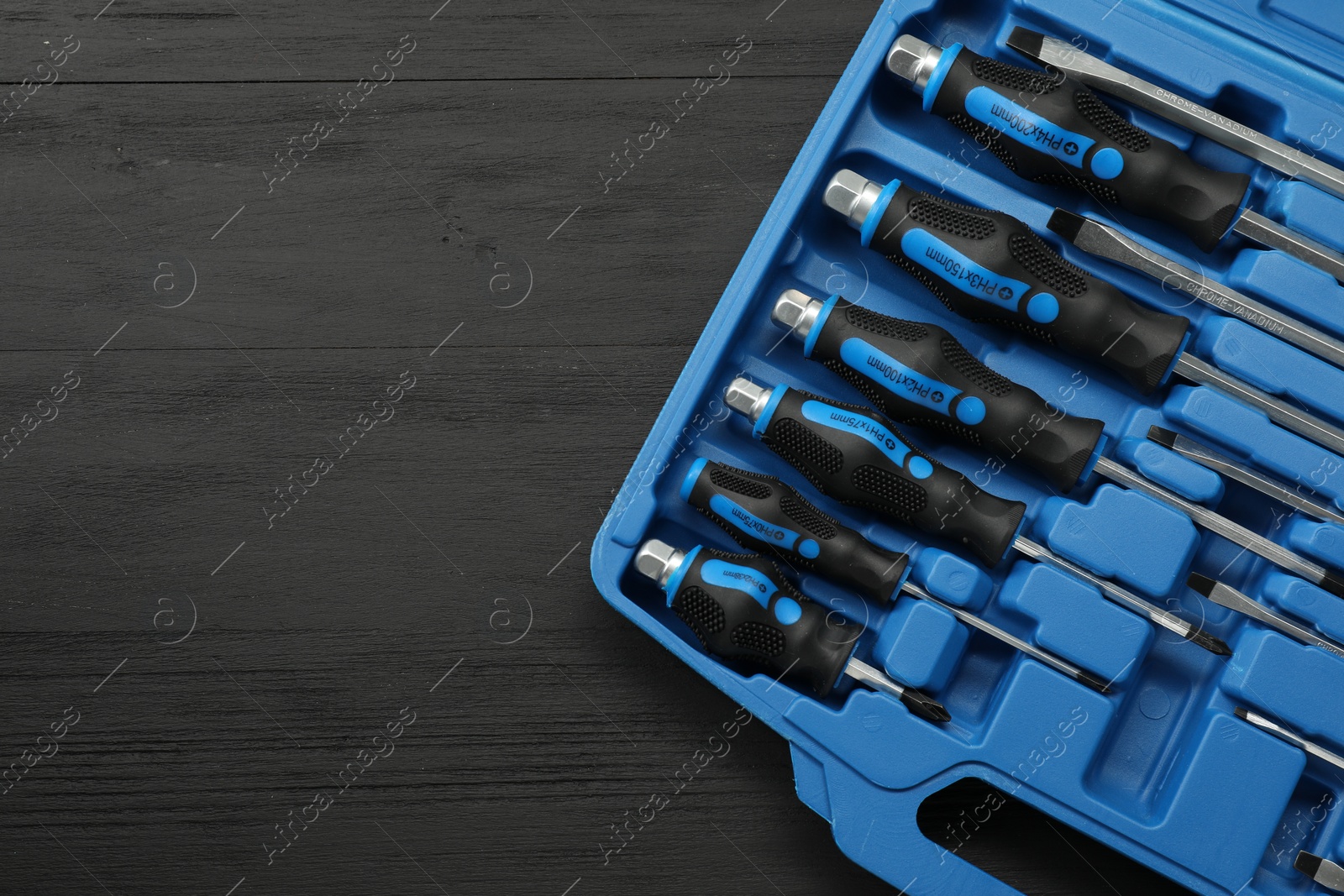 Photo of Set of screwdrivers in open toolbox on black wooden table, top view. Space for text