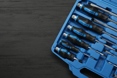 Photo of Set of screwdrivers in open toolbox on black wooden table, top view. Space for text