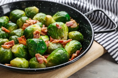 Tasty roasted Brussels sprouts with bacon on light grey table, closeup