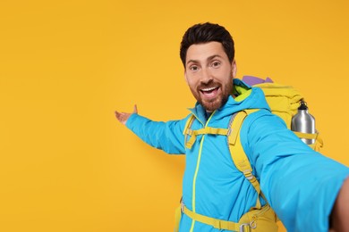 Photo of Happy man with backpack taking selfie on orange background, space for text. Active tourism