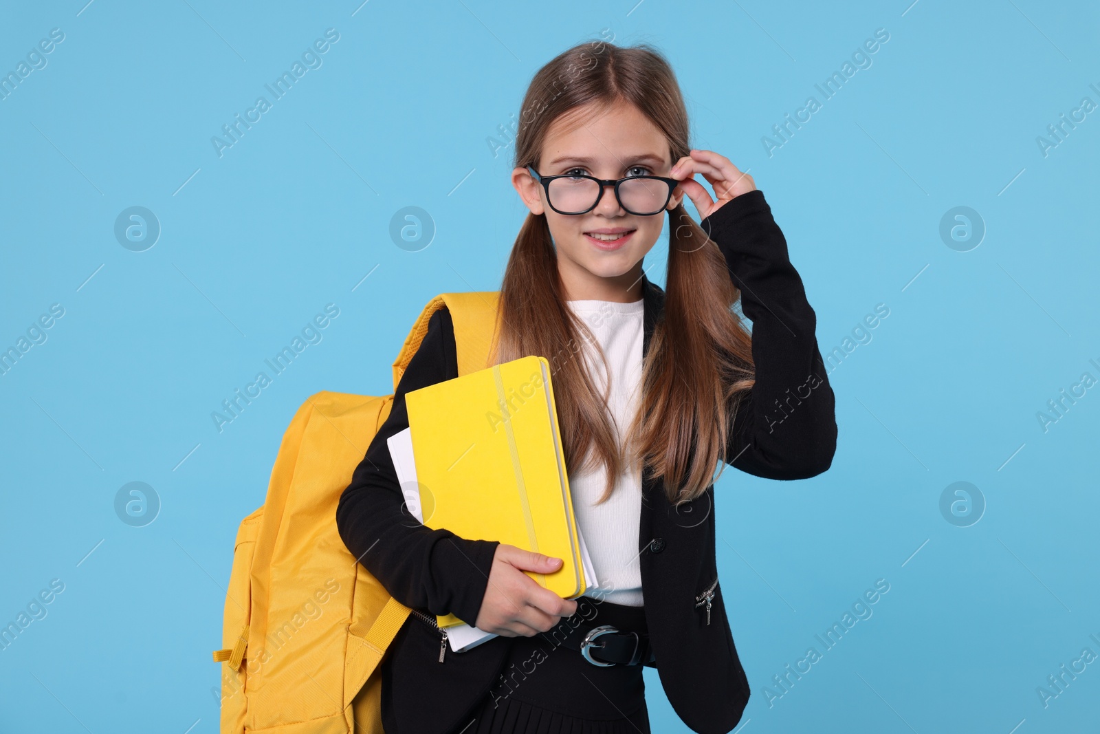 Photo of Happy schoolgirl with backpack and books on light blue background