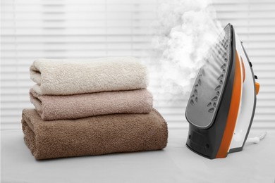 Image of Modern iron with steam and folded towels on ironing board