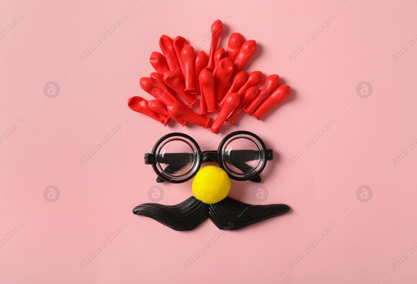 Photo of Funny face made with clown's accessories on pink background, flat lay