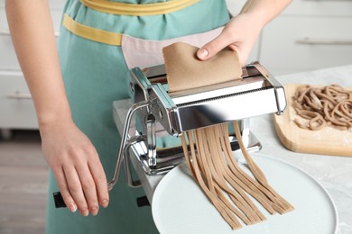 Photo of Woman preparing soba (buckwheat noodles) with pasta maker machine in kitchen, closeup