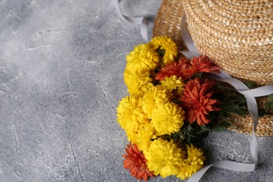 Bright chrysanthemum flowers and wicker hat on grey textured table, space for text