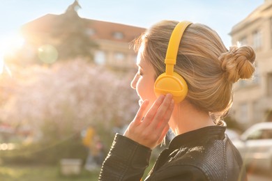 Photo of Young woman with headphones listening to music outdoors on sunny day, space for text