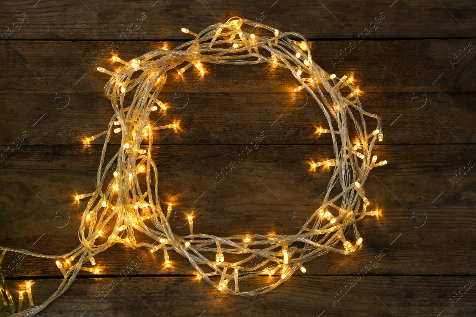 Photo of Frame made of glowing Christmas lights on wooden background, top view. Space for text