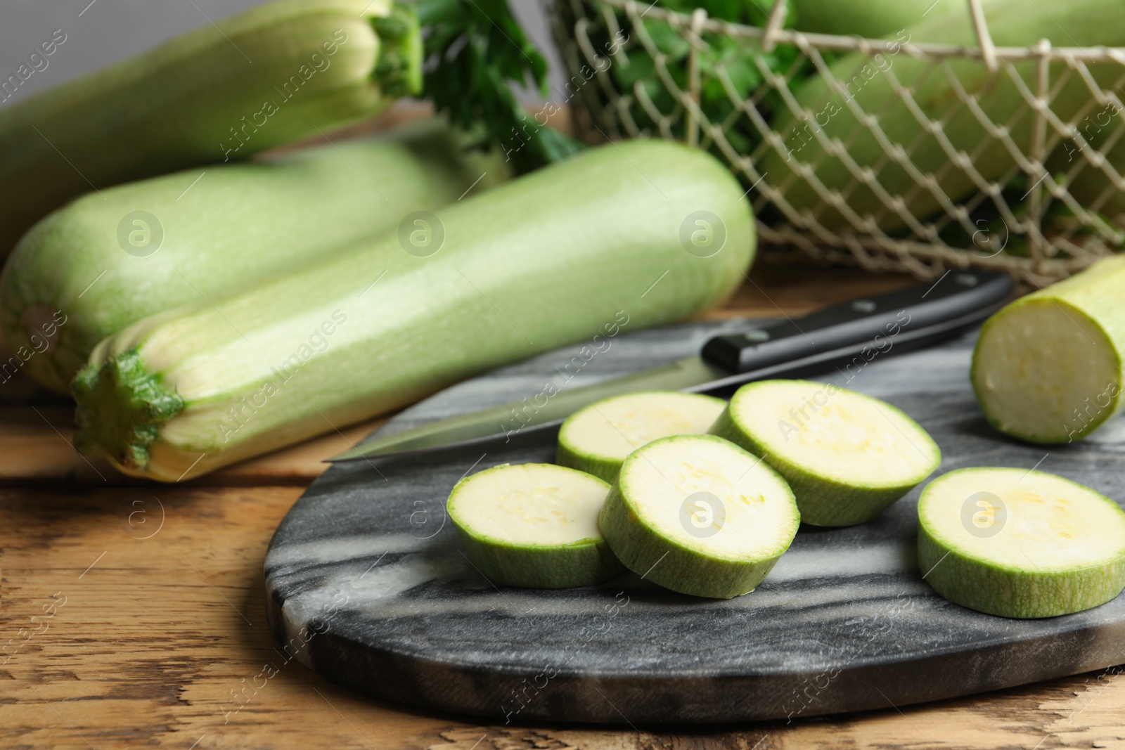 Photo of Sliced zucchini and grey marble board on wooden table, closeup