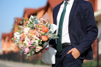 Man in stylish suit with beautiful flower bouquet on street, closeup view