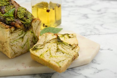 Photo of Freshly baked pesto bread with basil on white marble table, closeup. Space for text