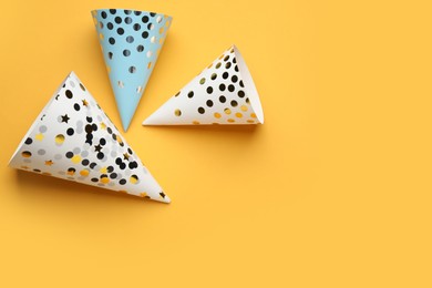 Photo of Bright party hats on orange background, flat lay. Space for text