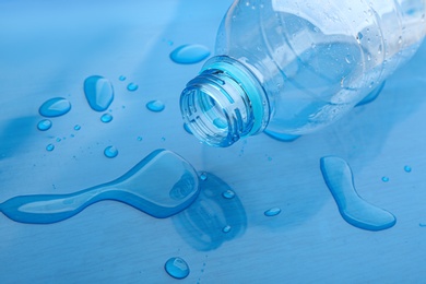 Photo of Drops of spilled water and plastic bottle on blue background, closeup