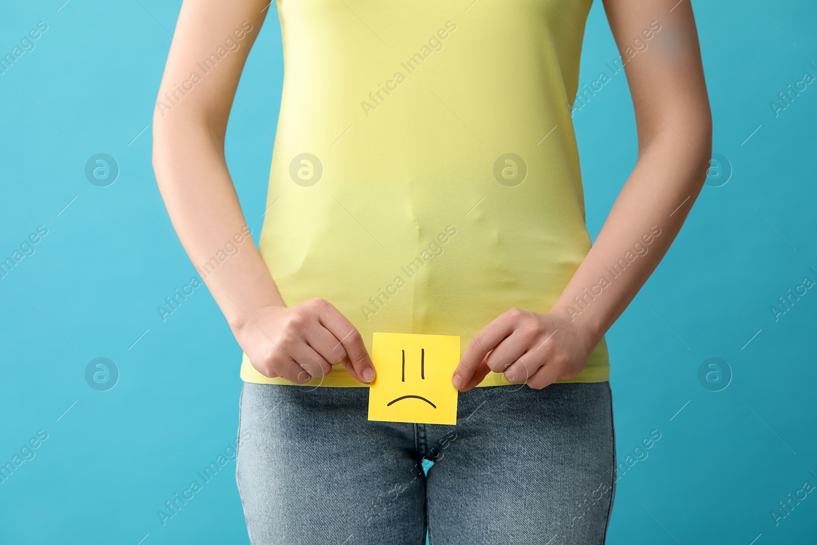 Photo of Cystitis. Woman holding sticky note with drawn sad face on light blue background, closeup