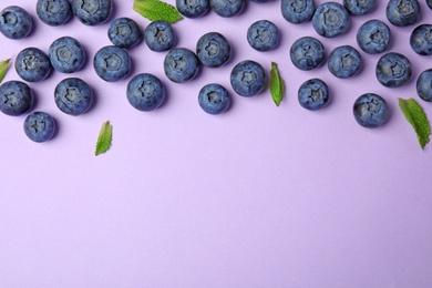 Tasty ripe blueberries and leaves on violet background, flat lay with space for text