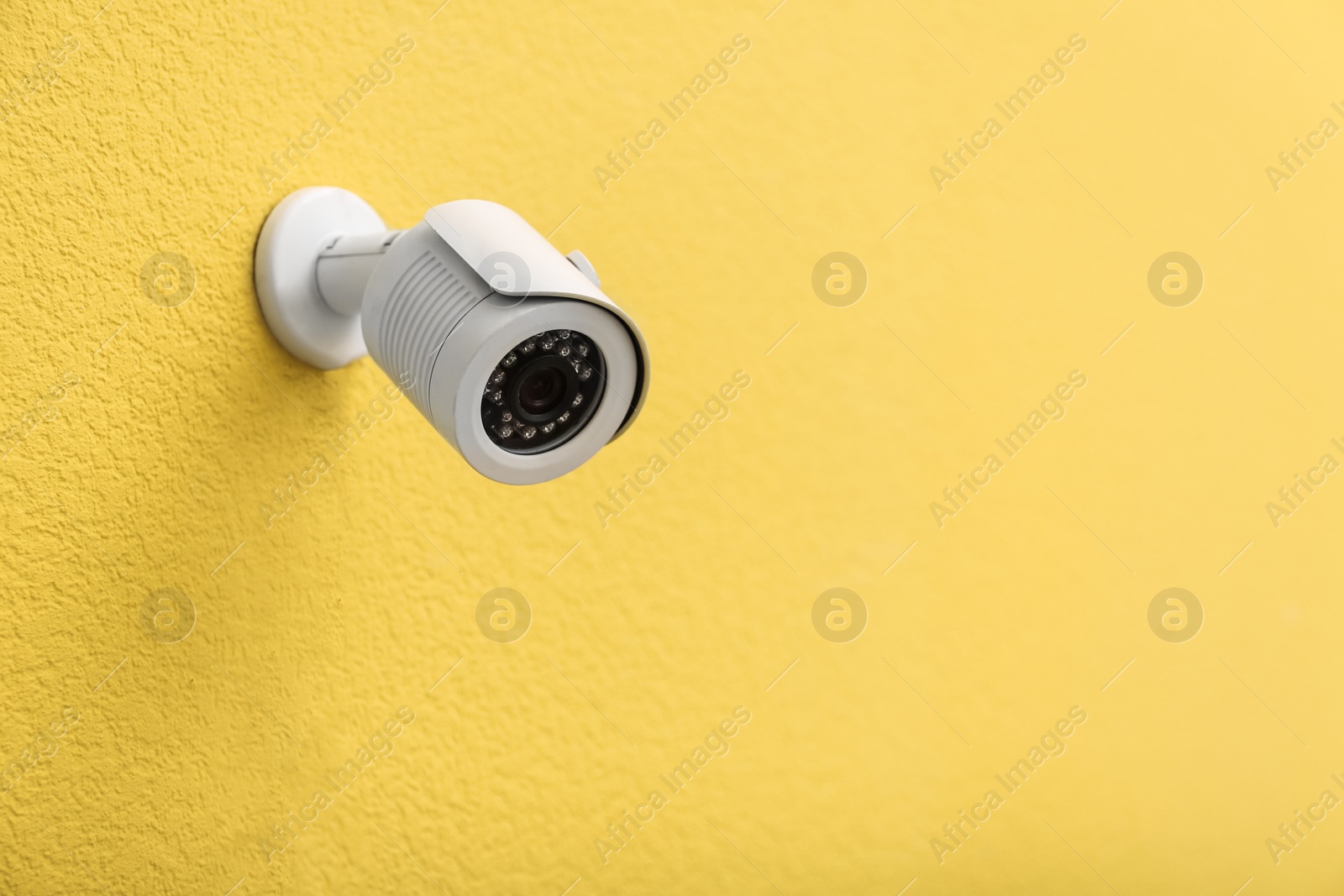 Photo of Modern CCTV security camera on yellow wall. Space for text