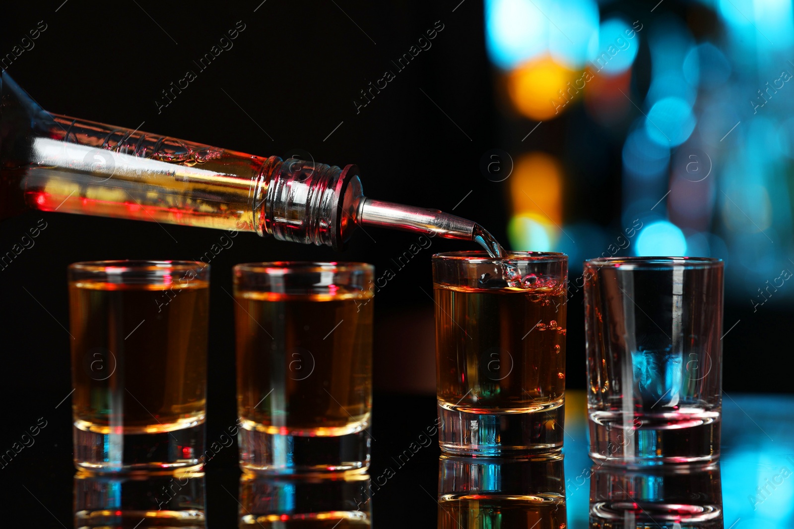 Photo of Pouring alcohol drink from bottle into shot glass at mirror bar counter, closeup