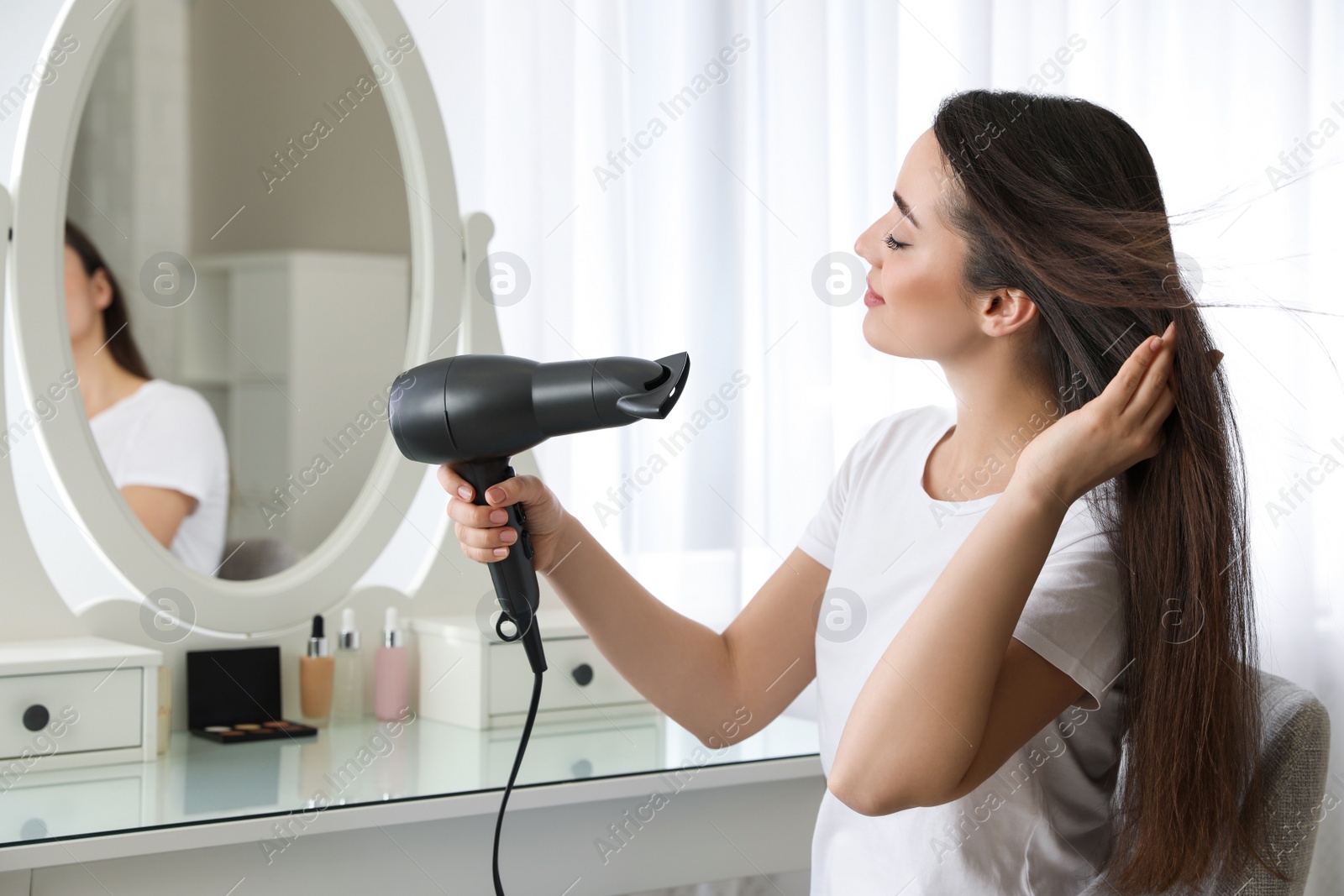 Photo of Beautiful young woman using hair dryer near mirror at home