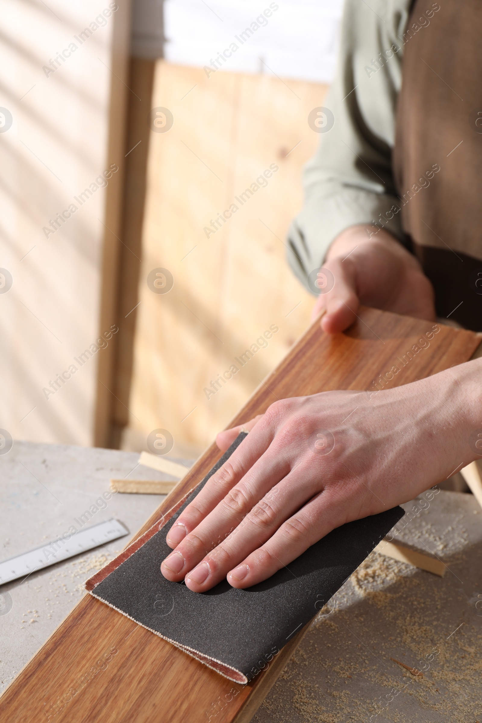 Photo of Man polishing wooden plank with sandpaper at grey table indoors, closeup