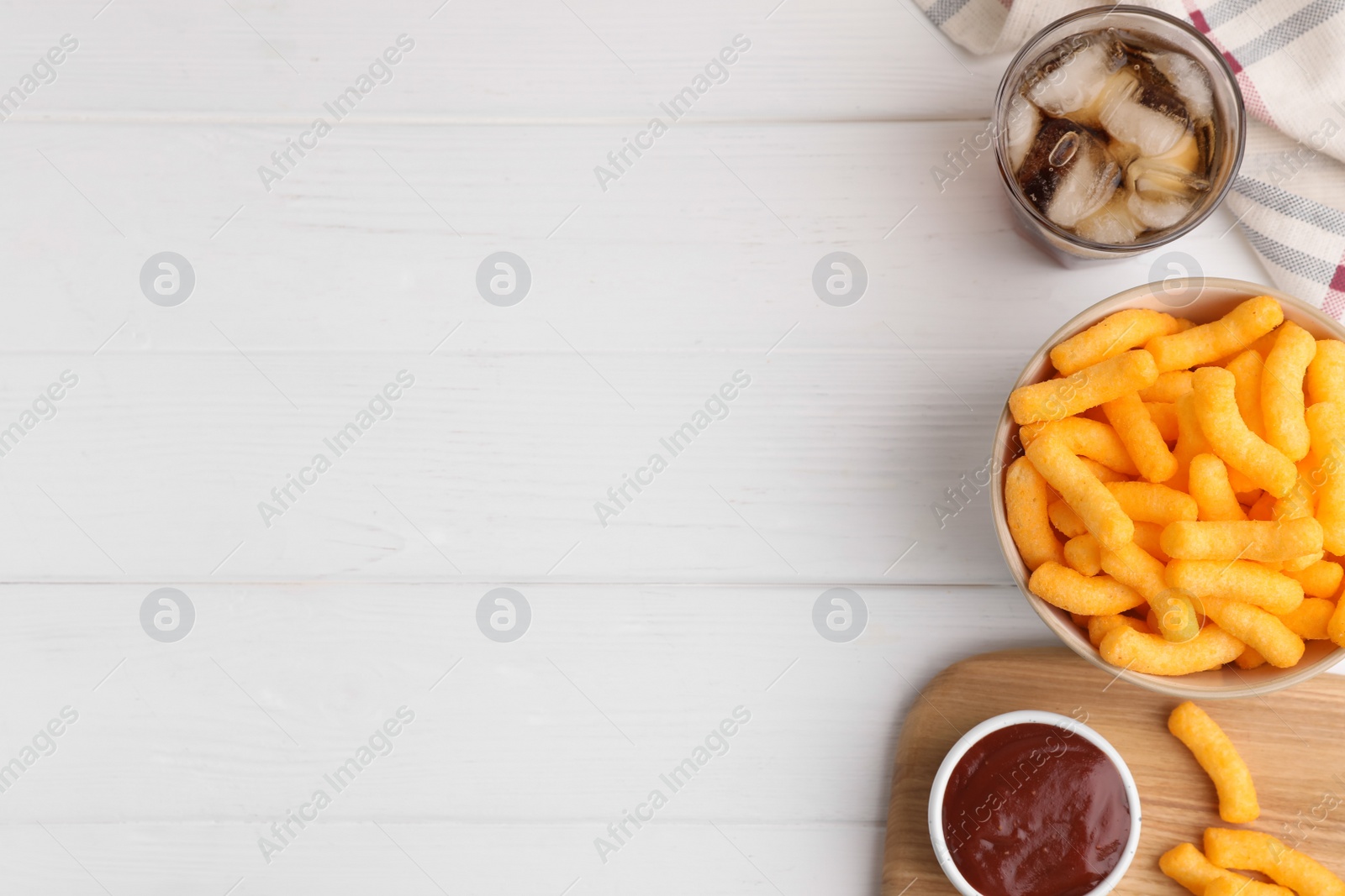 Photo of Crunchy cheesy corn snack, ketchup and refreshing drink on white wooden table, flat lay. Space for text