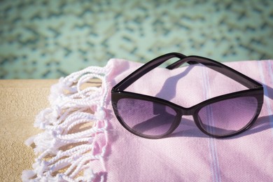 Photo of Stylish sunglasses and blanket near outdoor pool on sunny day, closeup. Space for text