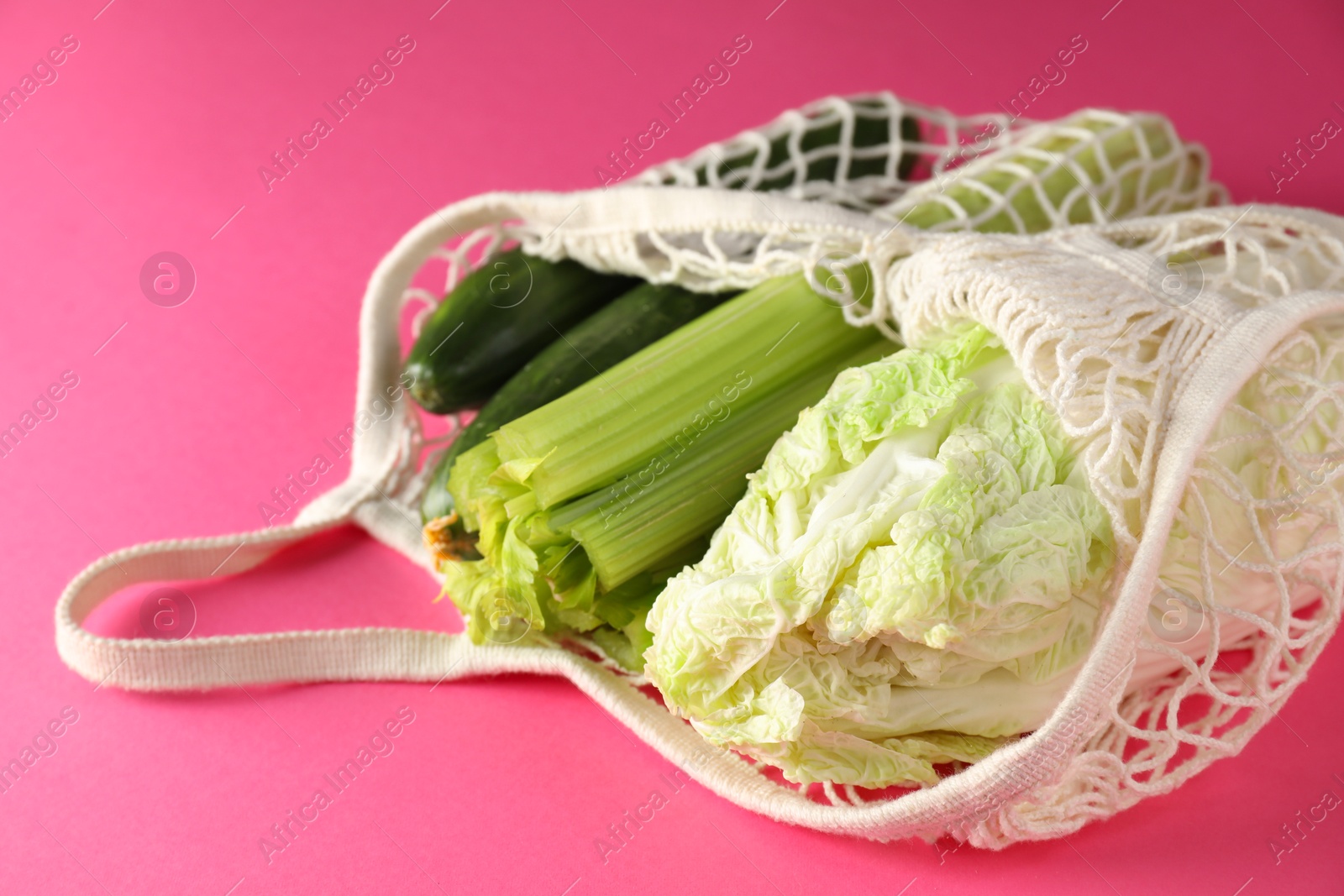 Photo of String bag with different vegetables on bright pink background, closeup