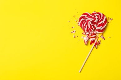 Photo of Broken heart shaped lollipop on yellow background, top view with space for text. Relationship problems concept