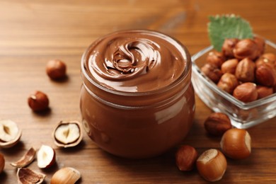 Photo of Glass jar with tasty chocolate hazelnut spread and nuts on wooden table