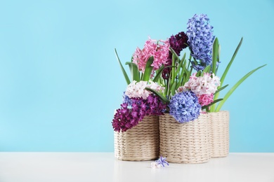 Photo of Beautiful hyacinths in wicker pots on table against color background, space for text. Spring flowers