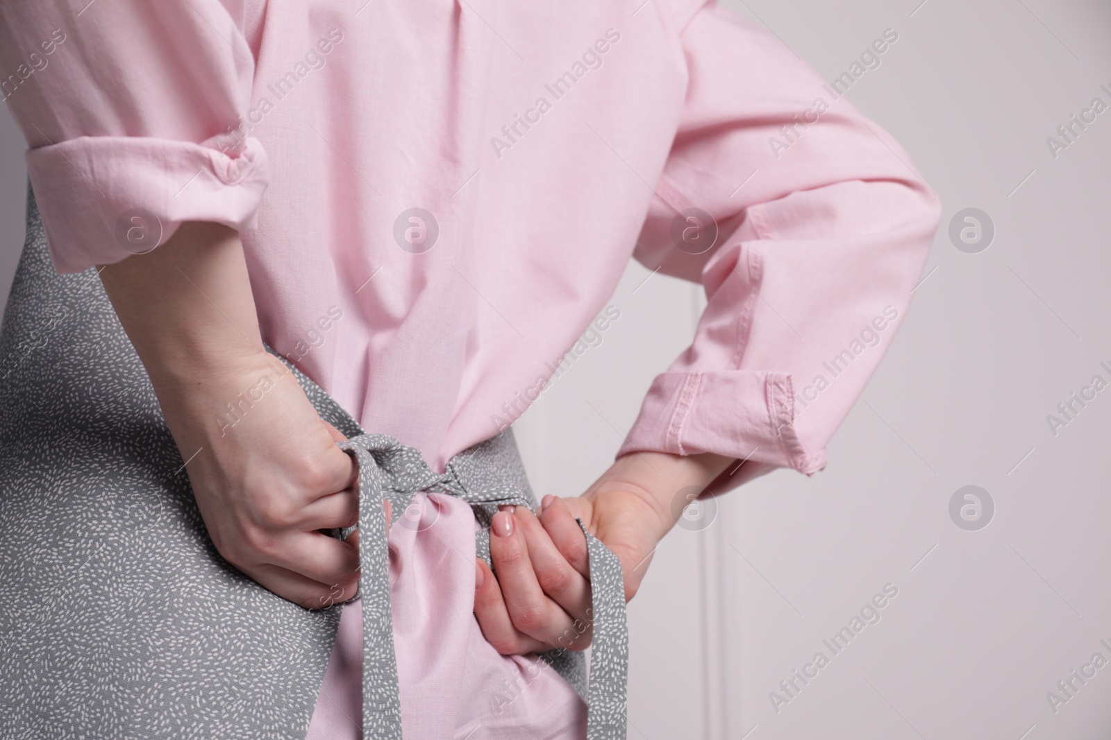 Photo of Woman putting on grey apron against white wall, closeup. Space for text