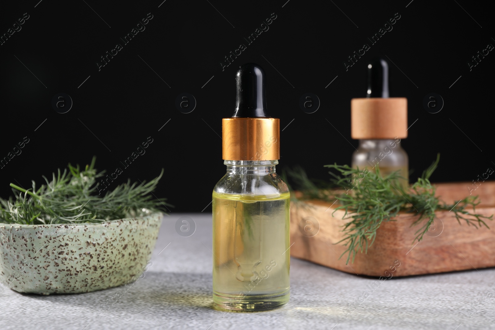 Photo of Bottles of essential oil and fresh dill on light grey table