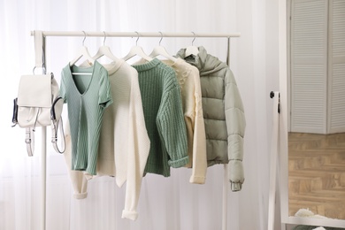 Rack with stylish warm clothes near mirror in dressing room