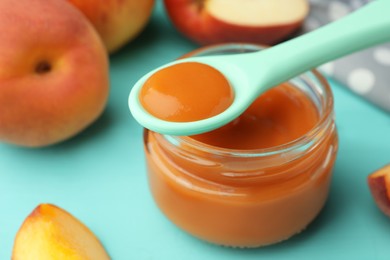 Spoon with healthy baby food over glass jar on turquoise table, closeup