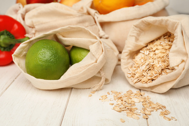 Cotton eco bags with fruits and oat flakes on white wooden table, closeup