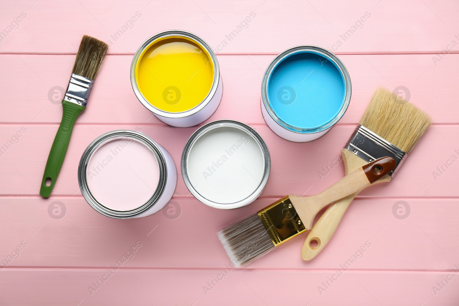 Photo of Cans of colorful paints with brushes on pink wooden table, flat lay