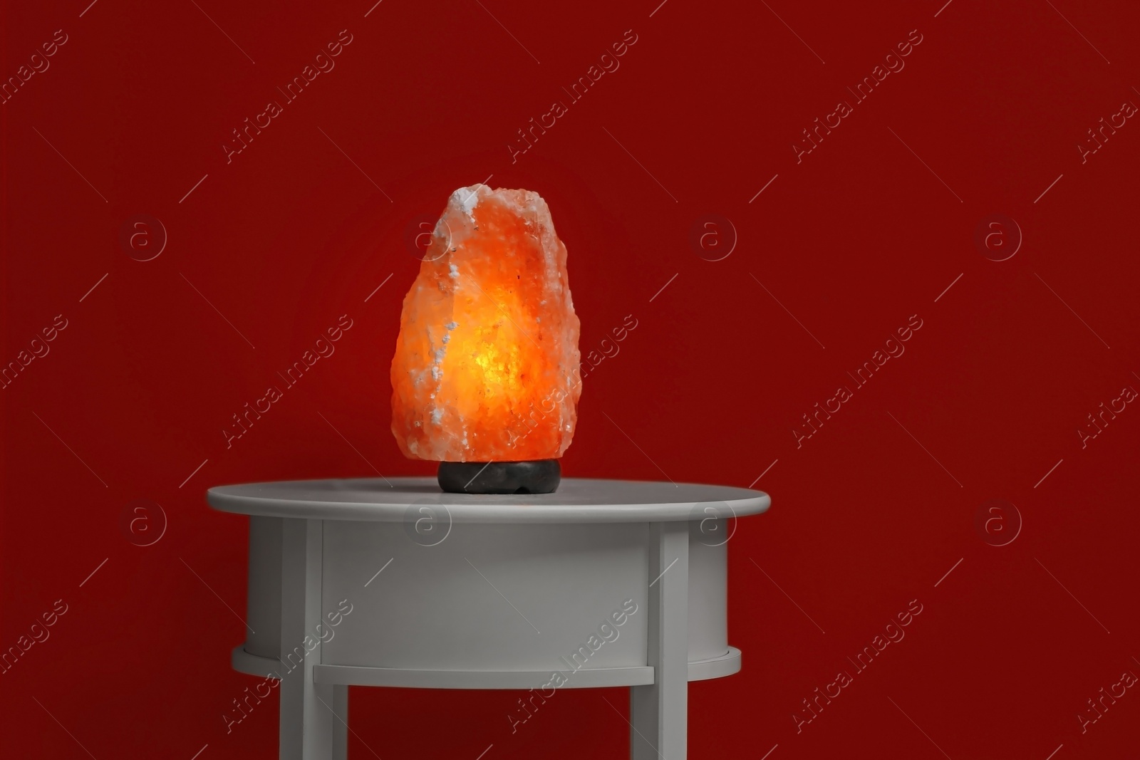 Photo of Himalayan salt lamp on table against dark red background